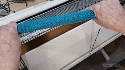 A knitter demonstrating the tubing technique, stretching a piece of machine-knitted fabric between both hands to help stitches settle into their natural position