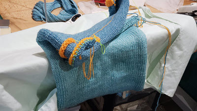 Machine knitting folded over needlebed to prevent stretching