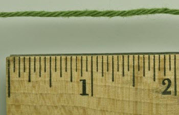 Close-up of yarn thickness measurement using a ruler, essential for machine knitting preparation