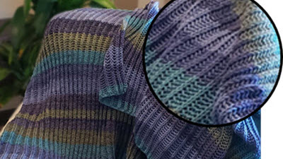 Close-up detail of a machine-knitted blanket in Fisherman Rib stitch, showing colorful self-striping yarn patterns and textured ribbing