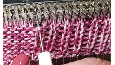 Demonstrating manual stitch reformation using a latch tool on a knitting machine, showing how to create ribbing by hand without a ribber attachment