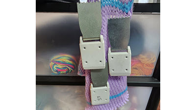 Several metal knitting machine claw weights hanging from a knitted swatch, demonstrating proper storage to protect their teeth and keep them easily accessible