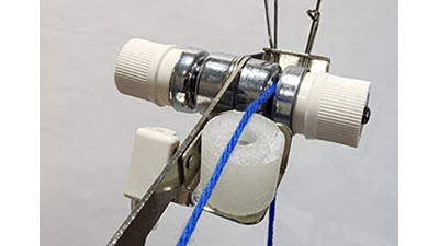 A Brother knitting machine's tension mast assembly showing a white wax ring positioned to coat yarn as it feeds through the system