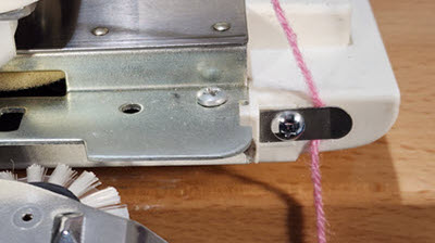 Close-up of a clip attached to a knitting machine's needle bed, holding a yarn tail securely to ensure proper stitch formation