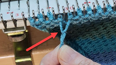 Close-up of a knitting machine bed showing a problematic yarn knot in the working yarn, demonstrating a common machine knitting issue