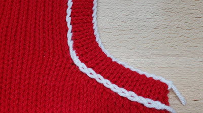 Close-up of a machine-knitted neckband showing decorative detail where the band meets the garment, demonstrating how to add visual interest to traditional band edges.