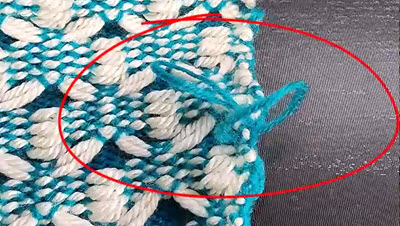 A close-up photo showing loose, uneven loops along the edge of a knitted fabric, demonstrating a common knitting machine error