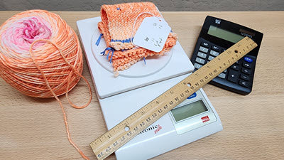 Knitting supplies: a ball of yarn, ruler, calculator, and a knitted swatch being weighed on a digital food scale