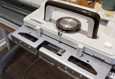 A knitting machine carriage positioned on the needle bed, ready for operation - a key component to inspect when buying a used machine