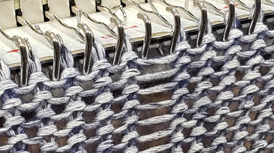 Close-up of machine knitted fabric showing highlighted ladder technique, where needles are deliberately left out of work for decorative effect