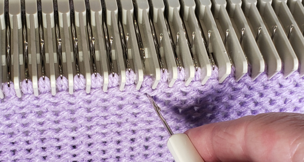Pull the machine needle back, dropping the stitch. Don't worry, because you've secured the stitch below with the latch tool, the dropped stitch won't run