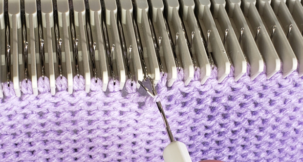 Position the new stitch behind the latch of the tool and place the hood over the hook of the needle on the machine