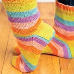 Colorful self-striping socks shown from the side, with one heel lifted to show the cuff, heel, and stripe progression.