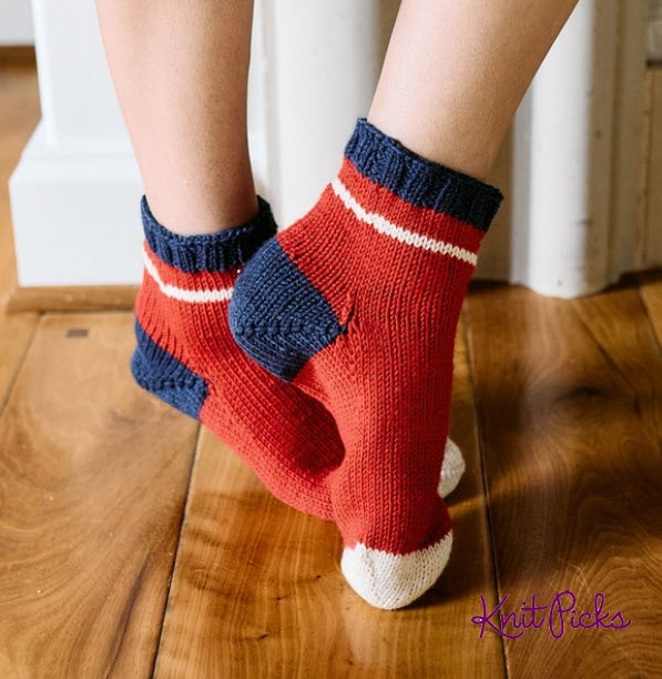 Red worsted-weight socks with navy cuffs and heels, cream toes, and narrow cream stripes.